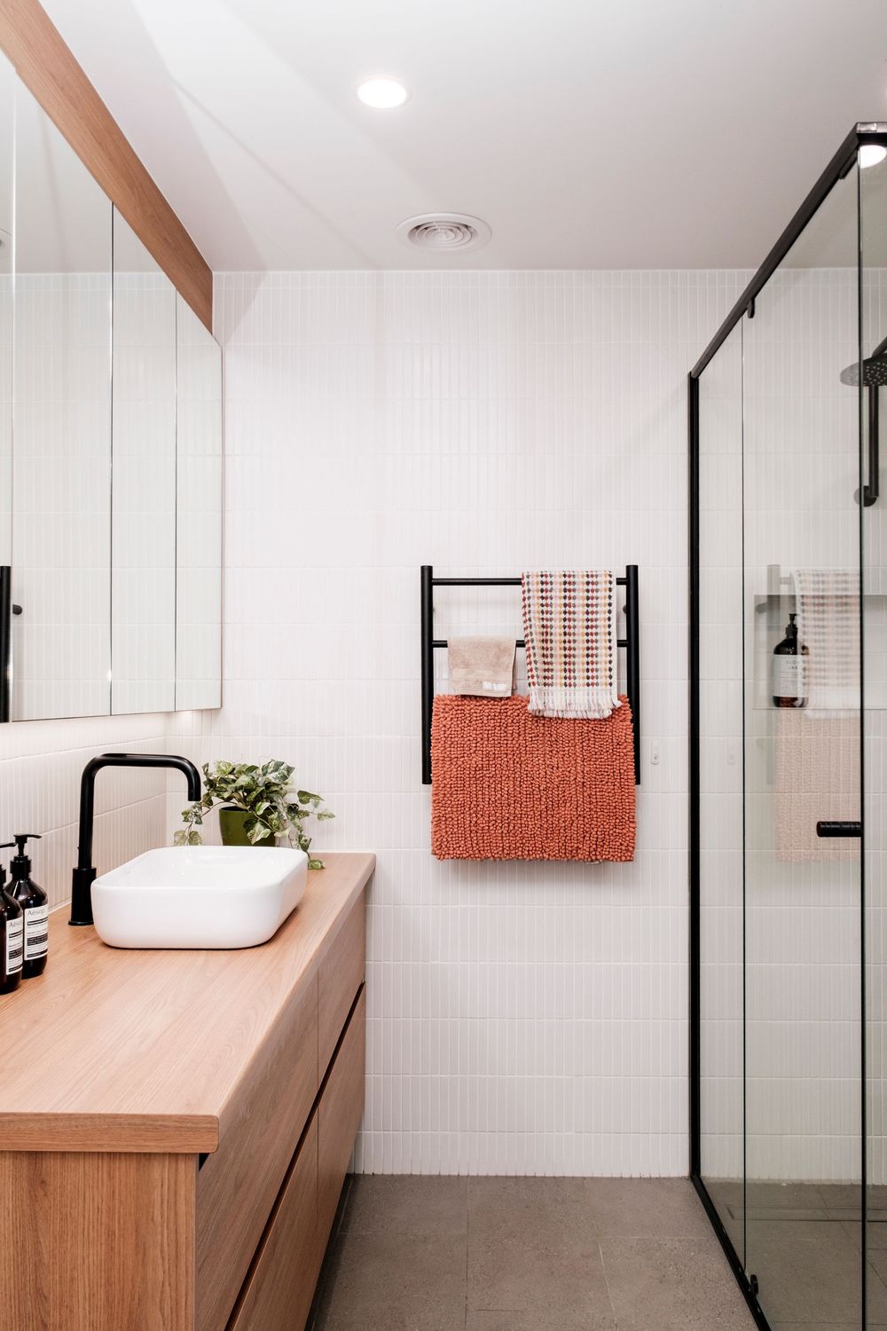 Modern bathroom with wooden vanity, white vessel sink, and black-framed glass shower partition.