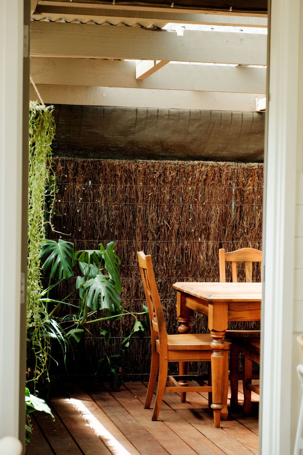 Covered outdoor dining area with wooden furniture and natural reed privacy screens.