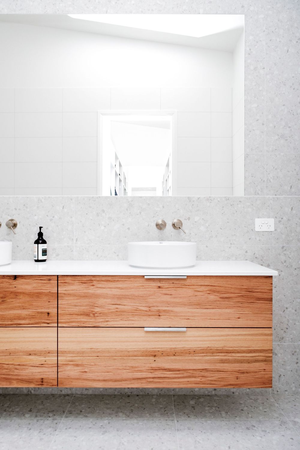 Minimalist floating wooden vanity with white countertop and wall-mounted black sconce.