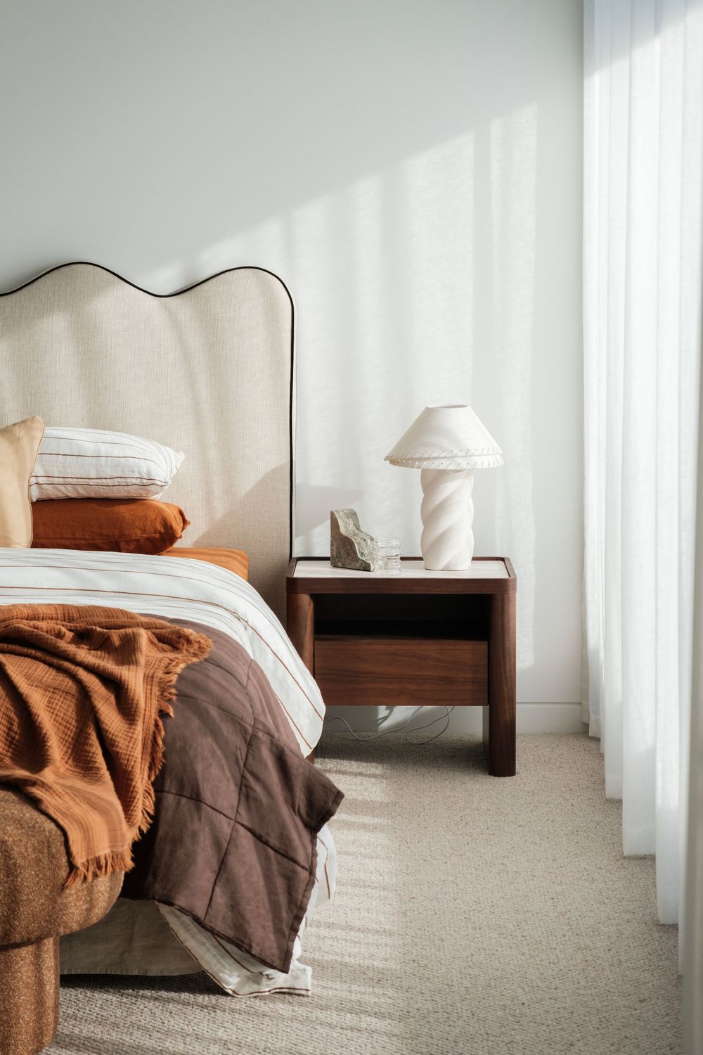 Cozy bedroom corner with brown bedding, curved headboard, and natural light filtering through curtains. 
Warrnambool, criterion, staging,