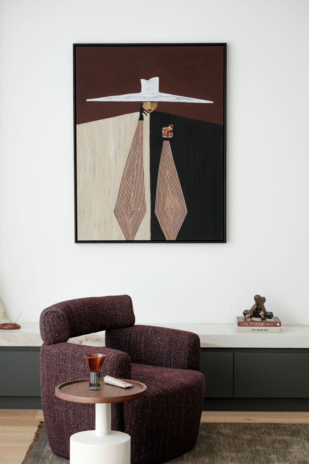 Modern living space with dark purple armchair and geometric artwork on white walls.