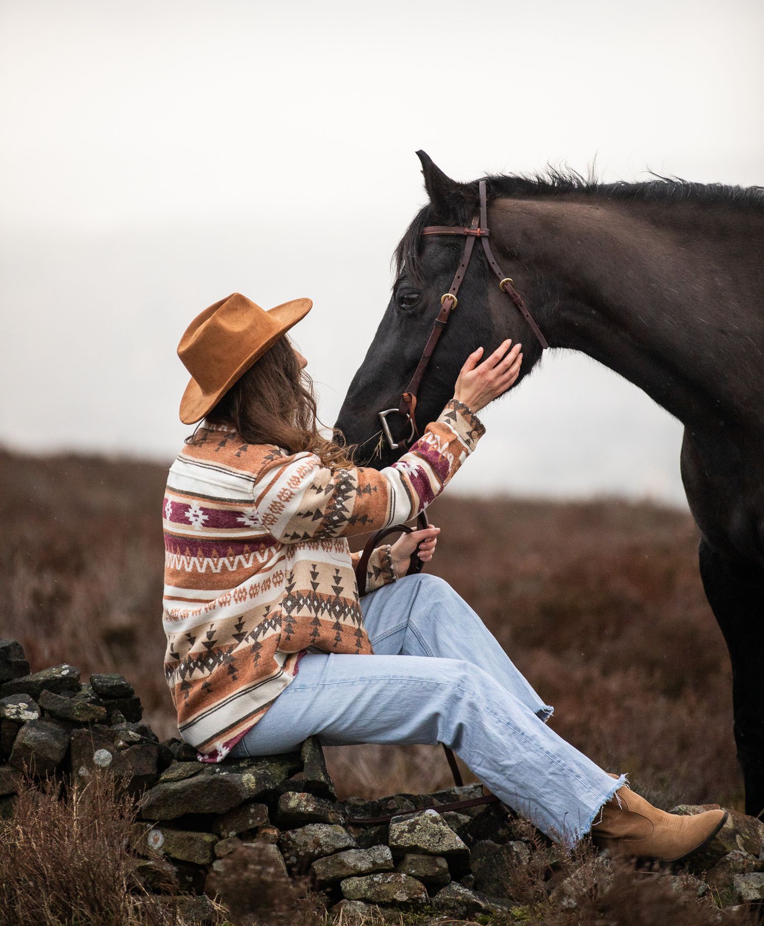 A majestic white horse stands with its handler amidst brown autumn hills during golden hour.