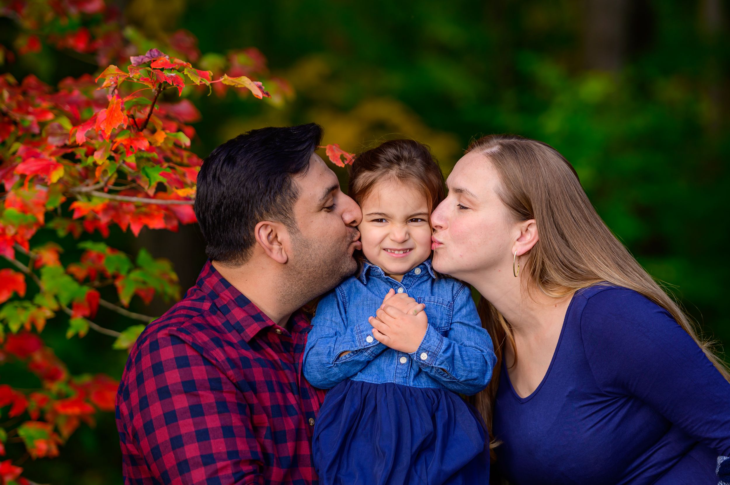 Family sharing tender moments together outdoors with vibrant red autumn foliage in the background at Audubon Society in Fairfield.