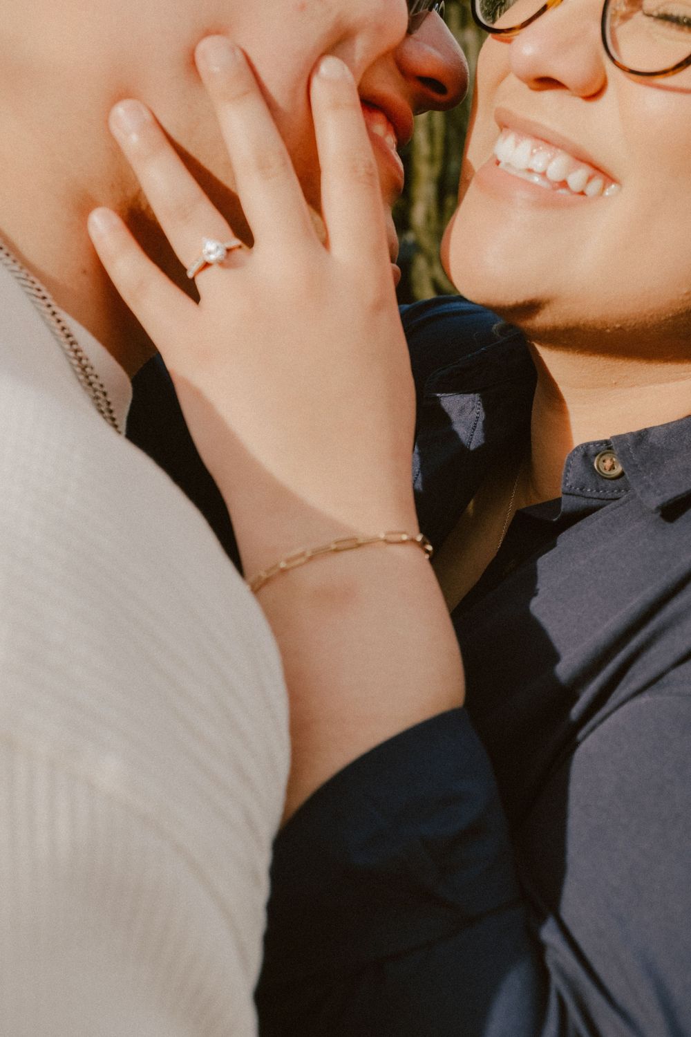 Close-up shot showing engagement ring and smiling faces in sunlight.