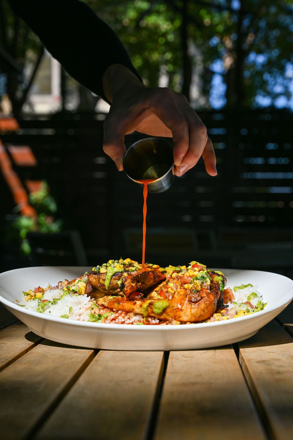 Chef drizzling orange sauce over a beautifully plated dish with garnishes on a white plate in natural lighting.