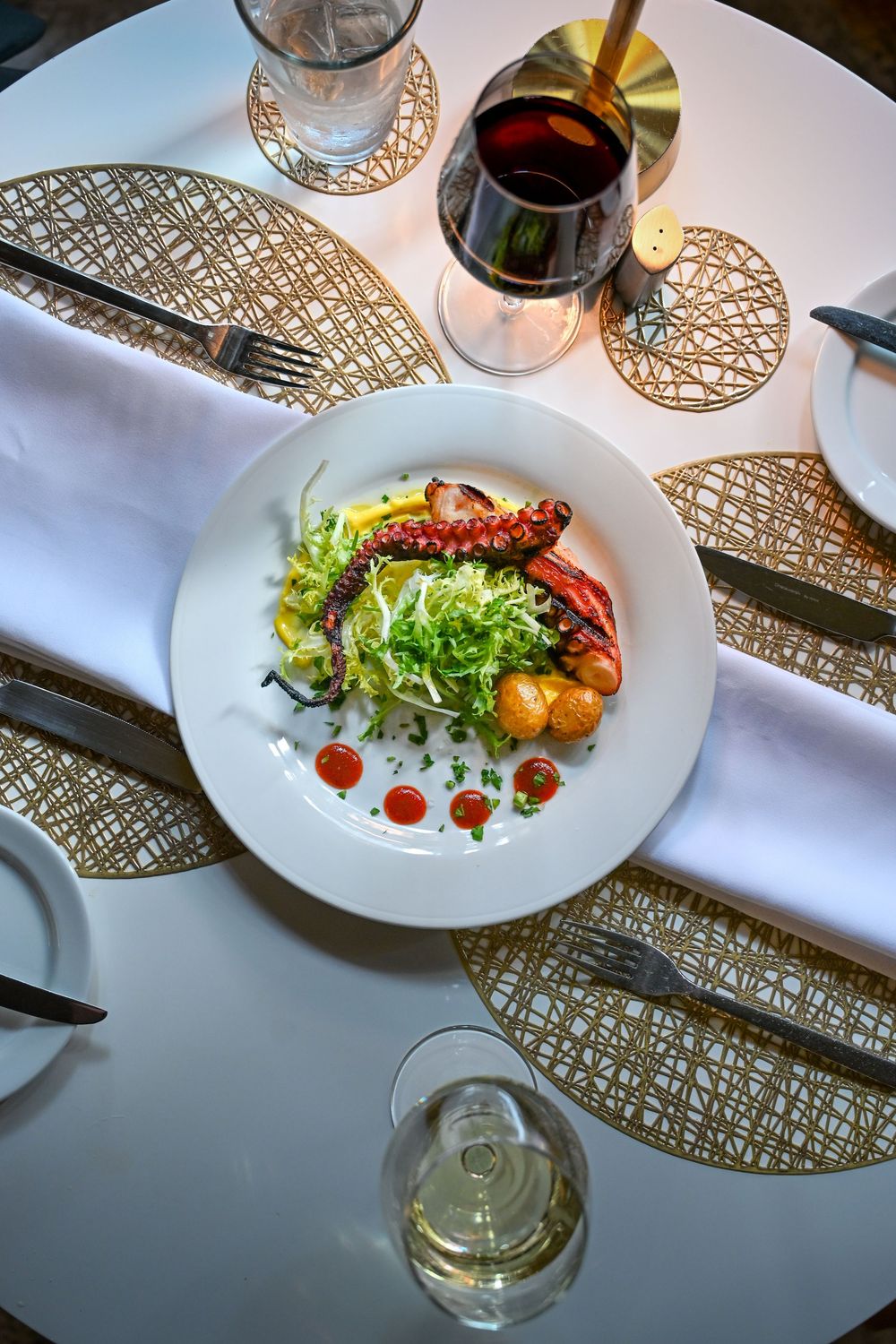 Elegant plated salad with shrimp on white dish alongside wine glasses and decorative gold placemats on white tablecloth.