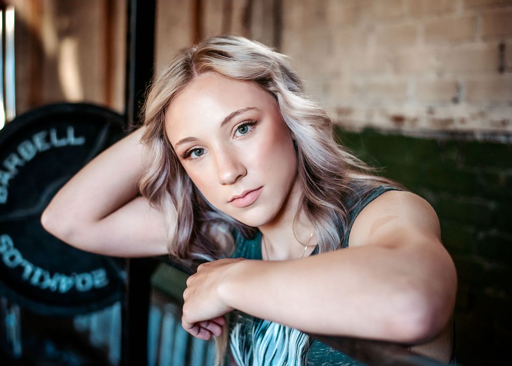 Young blonde woman rests on gym equipment during workout at a fitness facility.