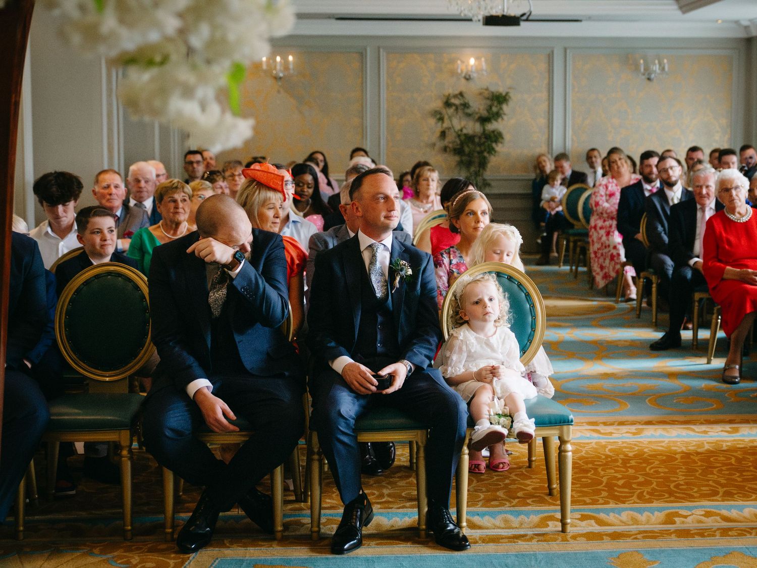 A joyful exchange of rings takes place during an elegant wedding ceremony under a crystal chandelier.