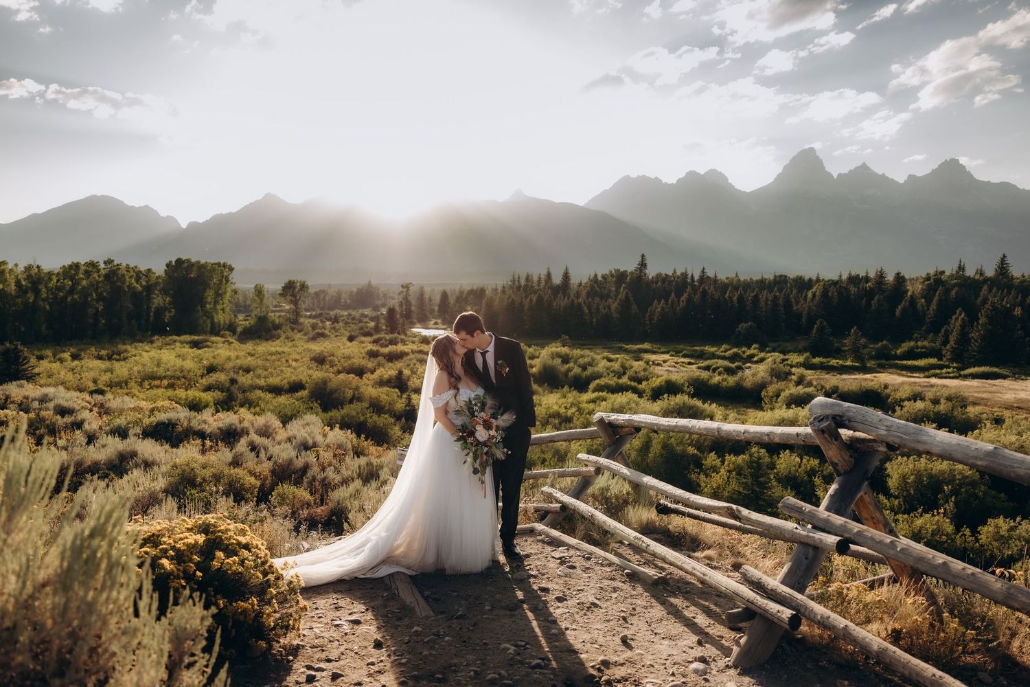 A newlywed couple stands beneath a grand antler arch at their rustic outdoor wedding venue.