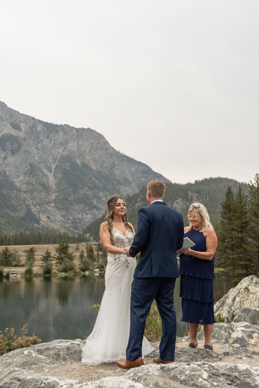Wedding ceremony on a rocky outcrop overlooking a serene mountain lake and rugged peaks in a scenic outdoor setting.