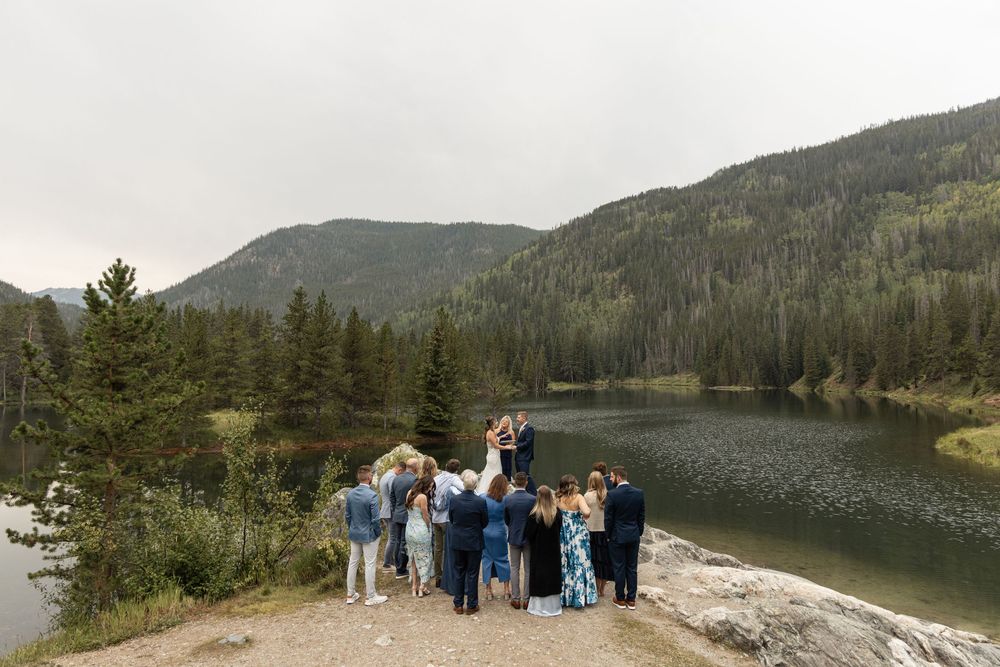 Scenic panoramic mountain vista overlooking a serene mountain lake surrounded by dense forest and rocky terrain.