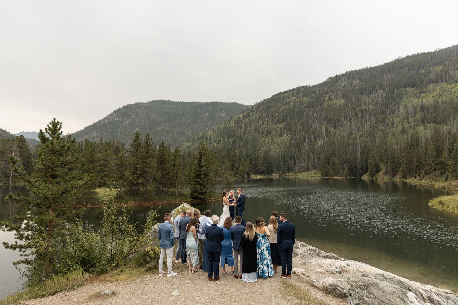 Scenic panoramic mountain vista overlooking a serene mountain lake surrounded by dense forest and rocky terrain.