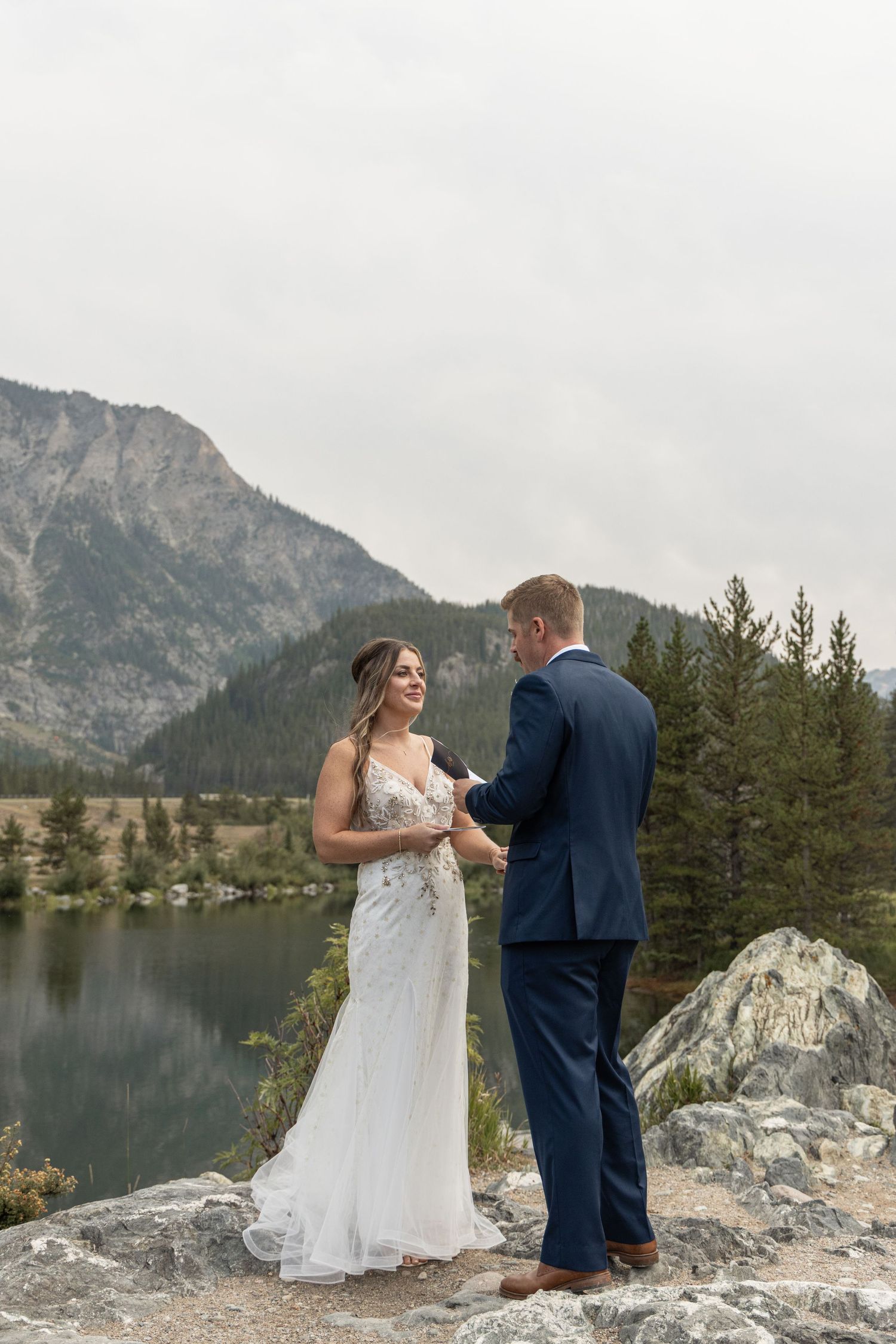 Scenic mountain wedding photography sequence on a rocky outcrop overlooking an alpine lake with evergreen trees.