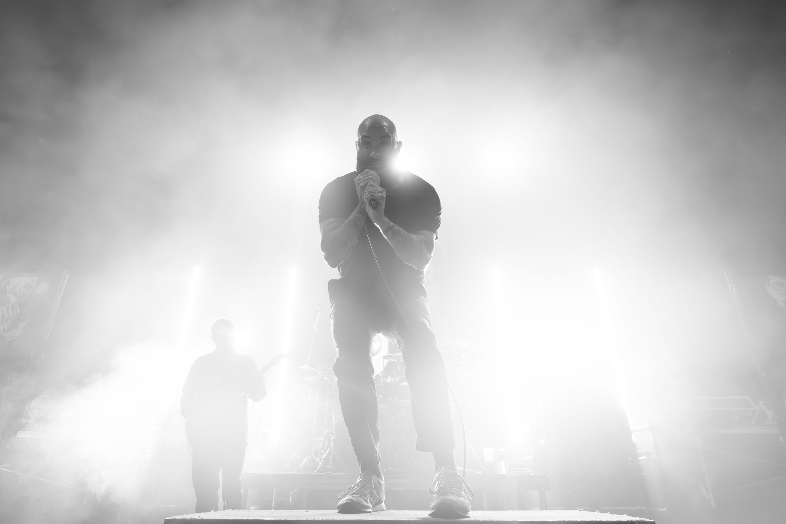 Dramatic black and white silhouettes of performers on a fog-filled stage with bright backlighting.