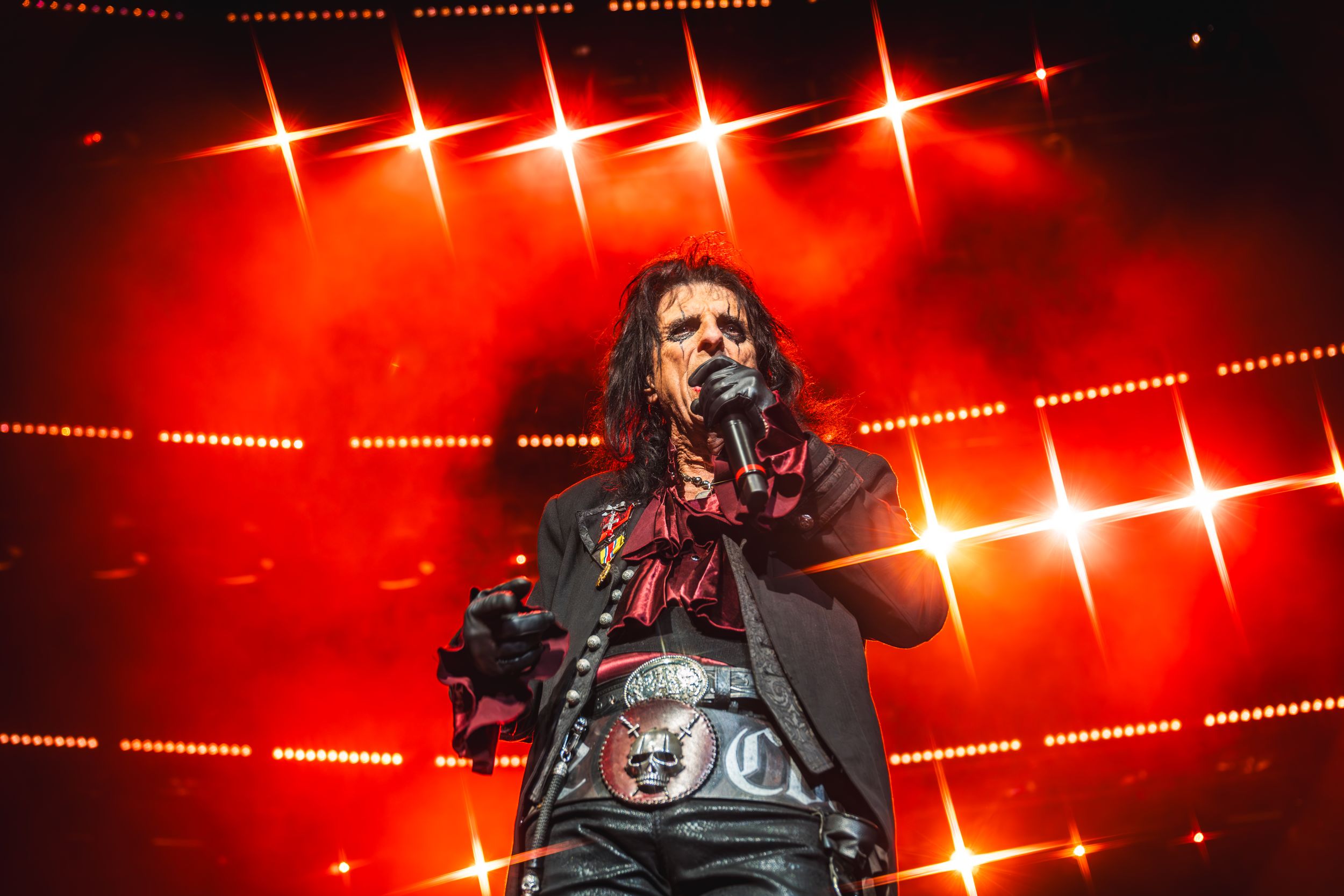 Concert performance with dramatic red spotlights and star-burst lighting effects.