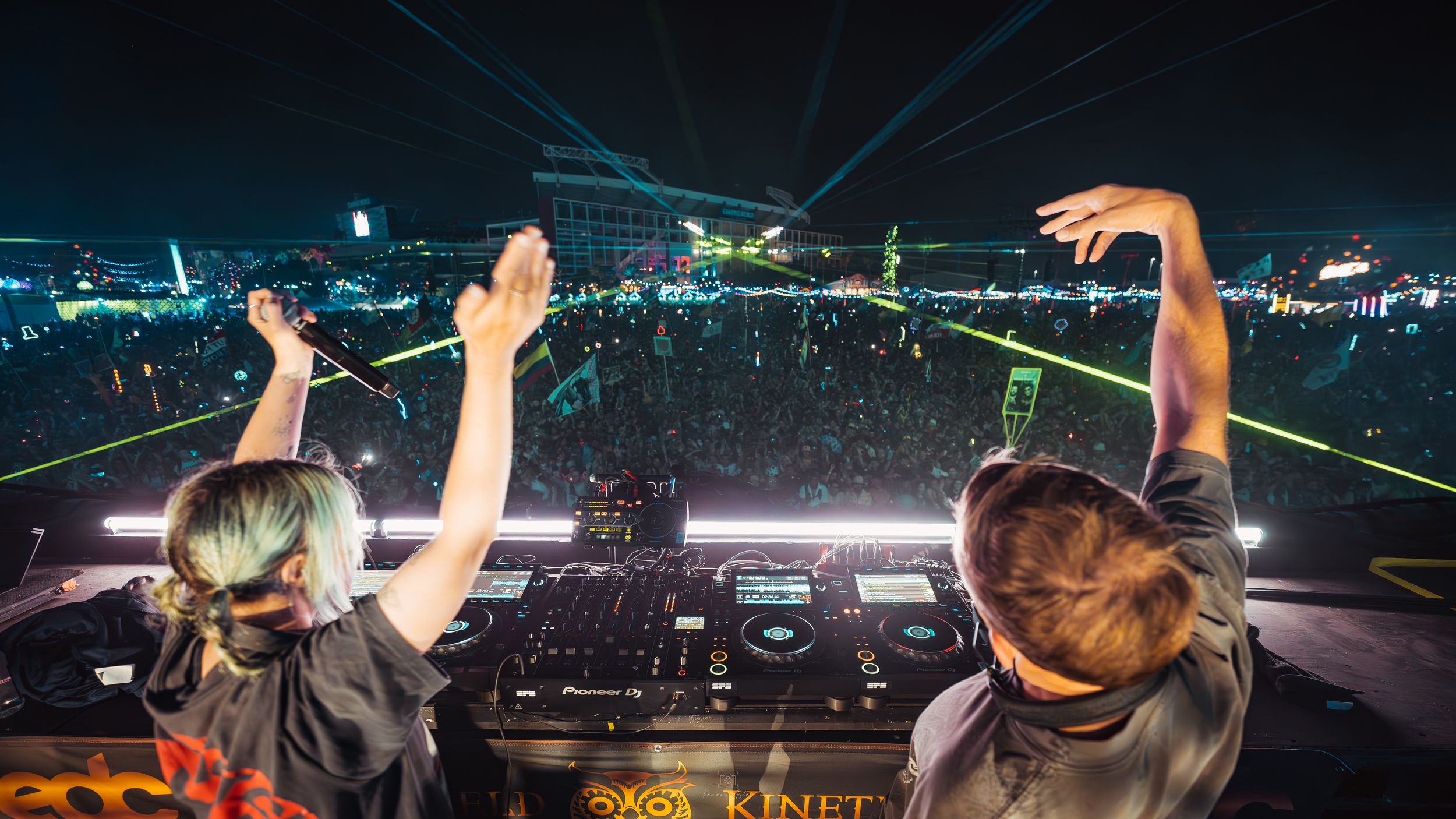 Aerial view of concert venue with colorful laser beams cutting through the night sky.