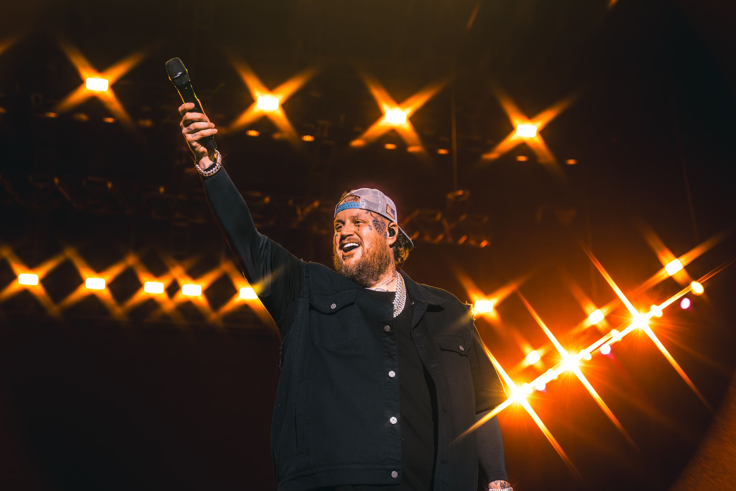 Concert performer raising arm against dramatic stage lighting with starburst effects in dark venue.