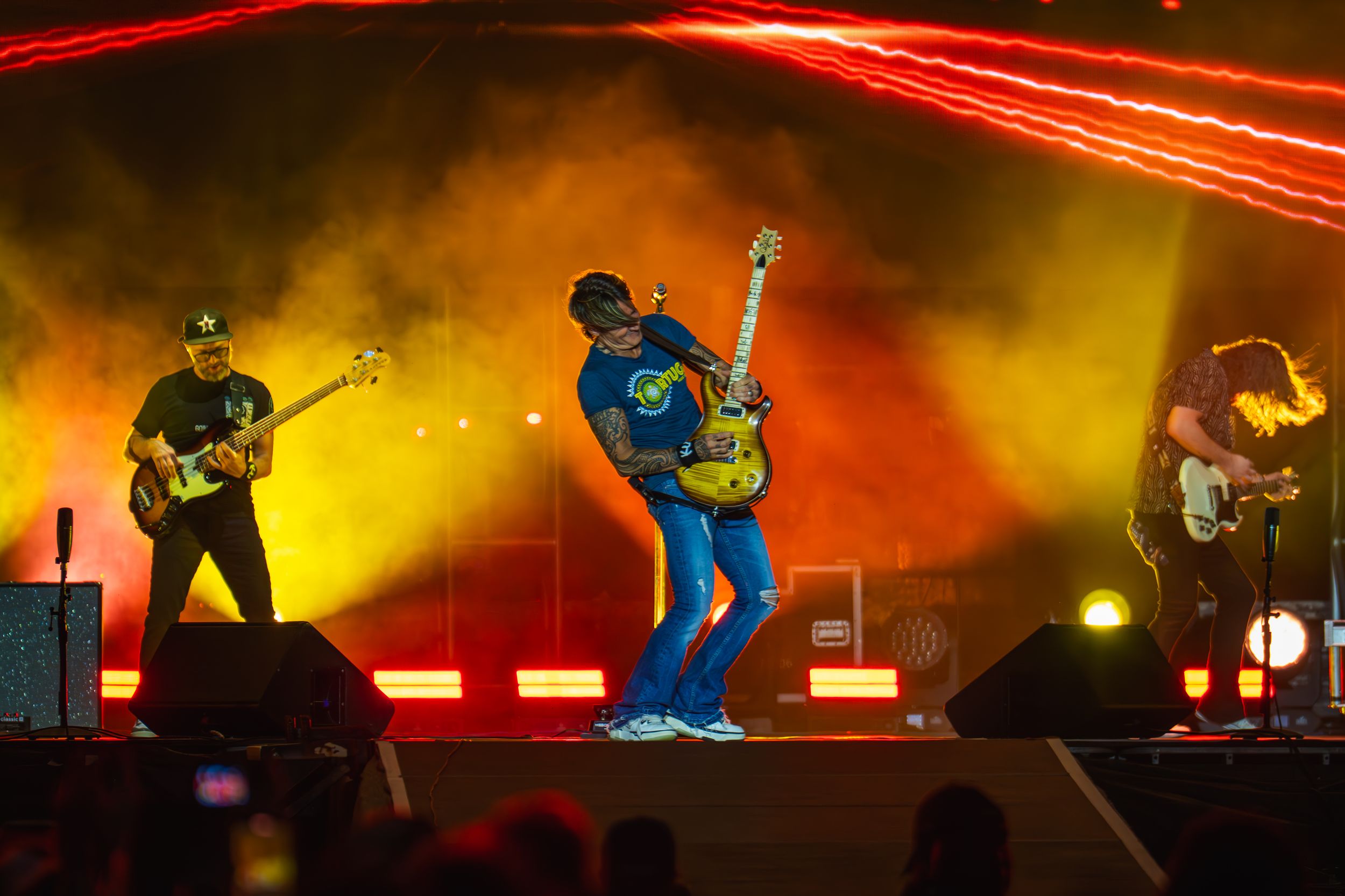 Band performing on stage with red lighting effects and guitarists in dramatic poses.