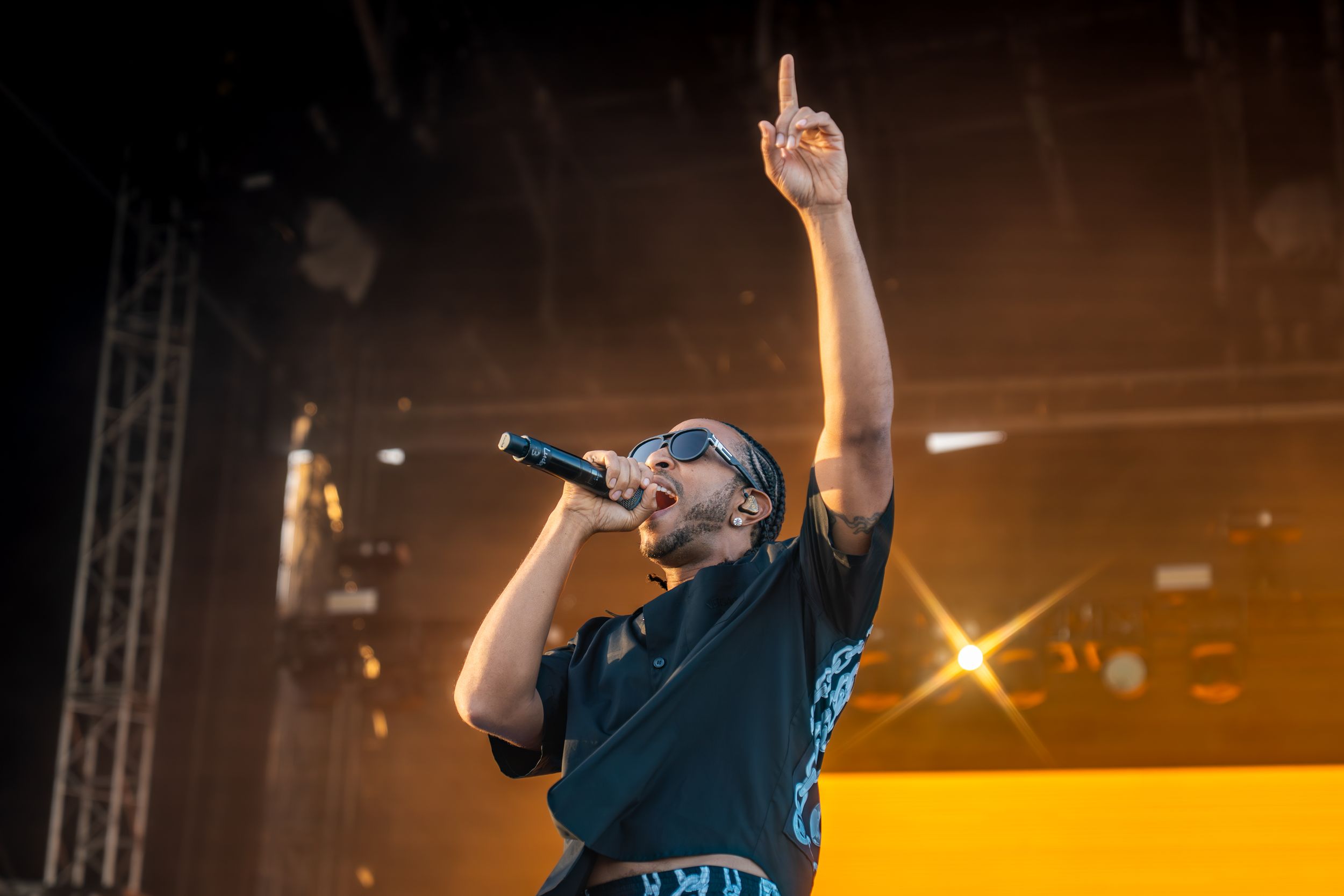 Concert performer holding microphone with raised arm on illuminated stage.