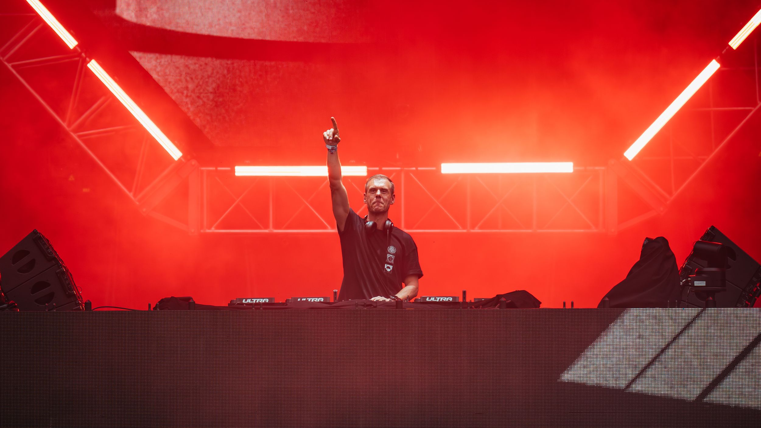 DJ performing at deck station with bright red lighting and geometric stage design.