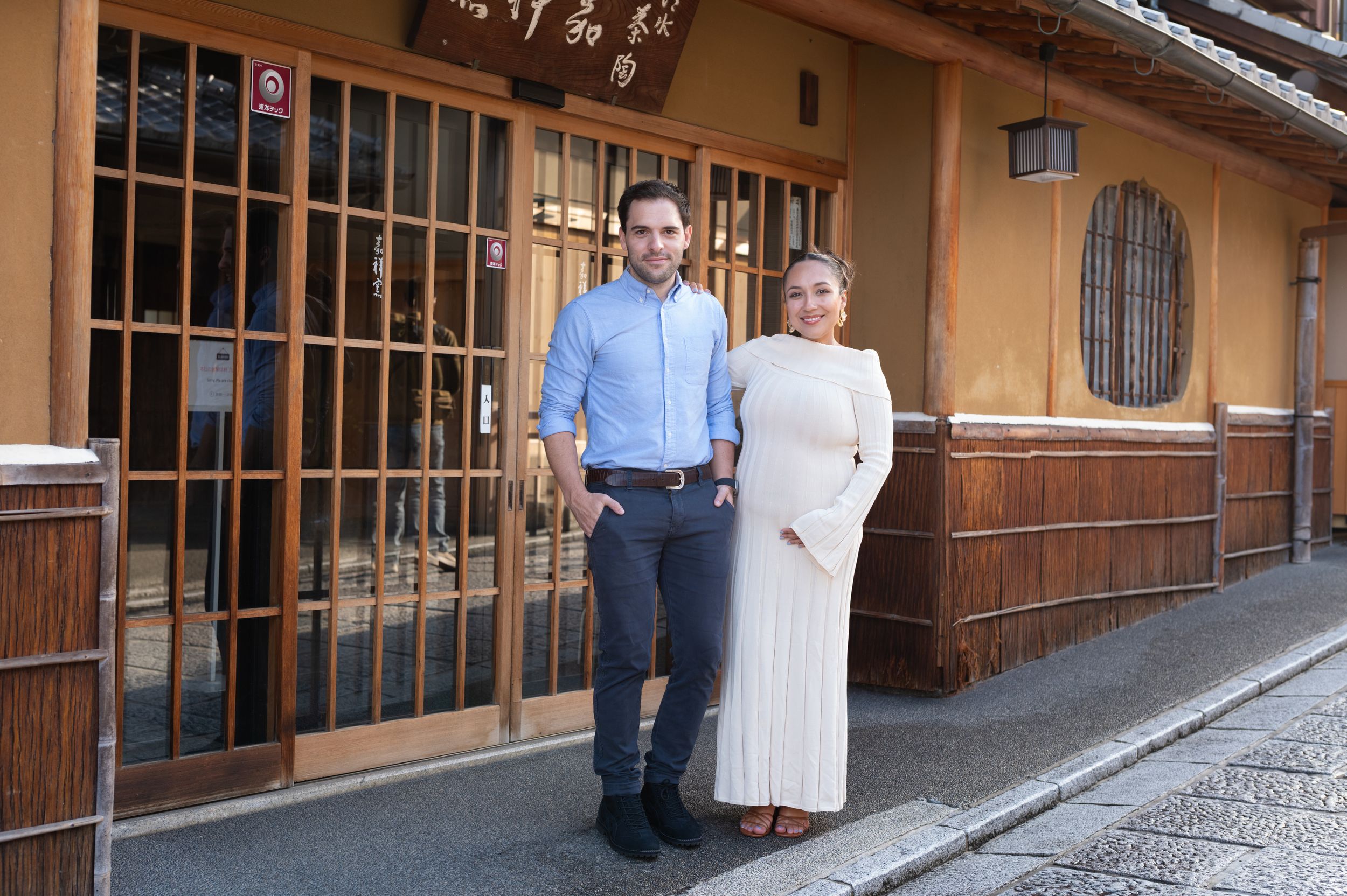 Pregnant couple poses together on a traditional Japanese street in front of a wooden storefront.