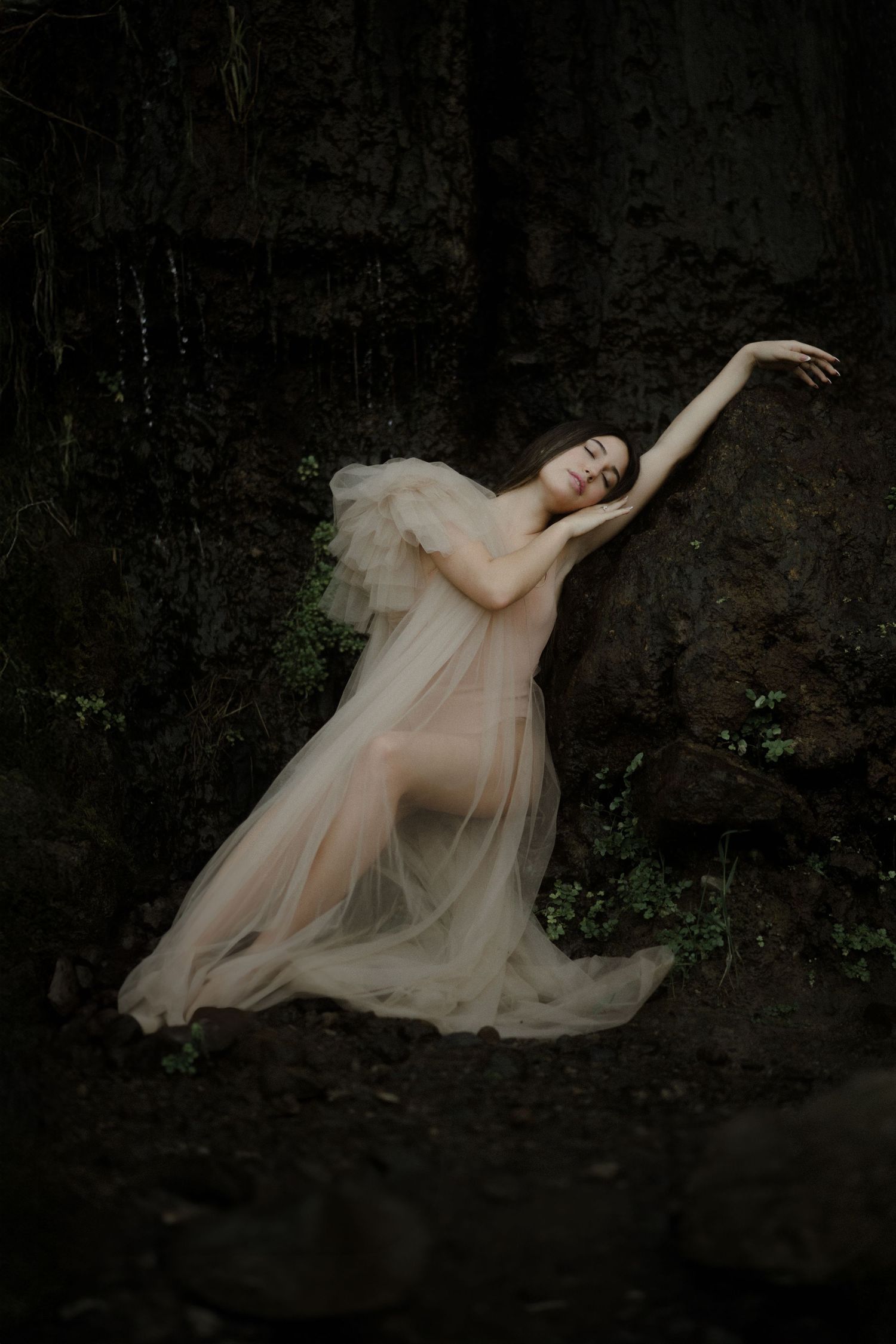 Romantic dark and moody portraits against black rocks with figure in flowing champagne gown.
