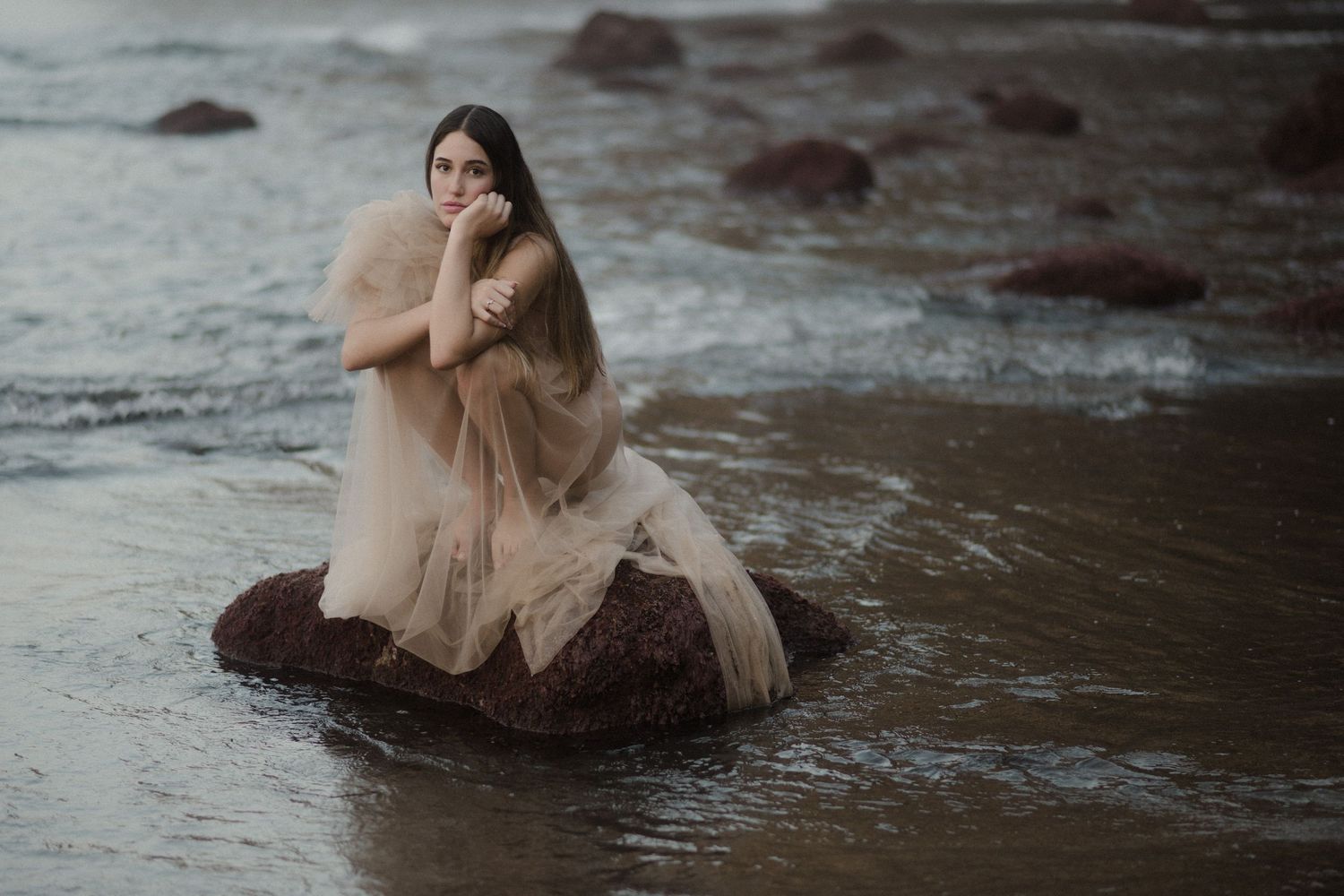 Moody water scene with soft figure in light dress sitting among rippling reflections.