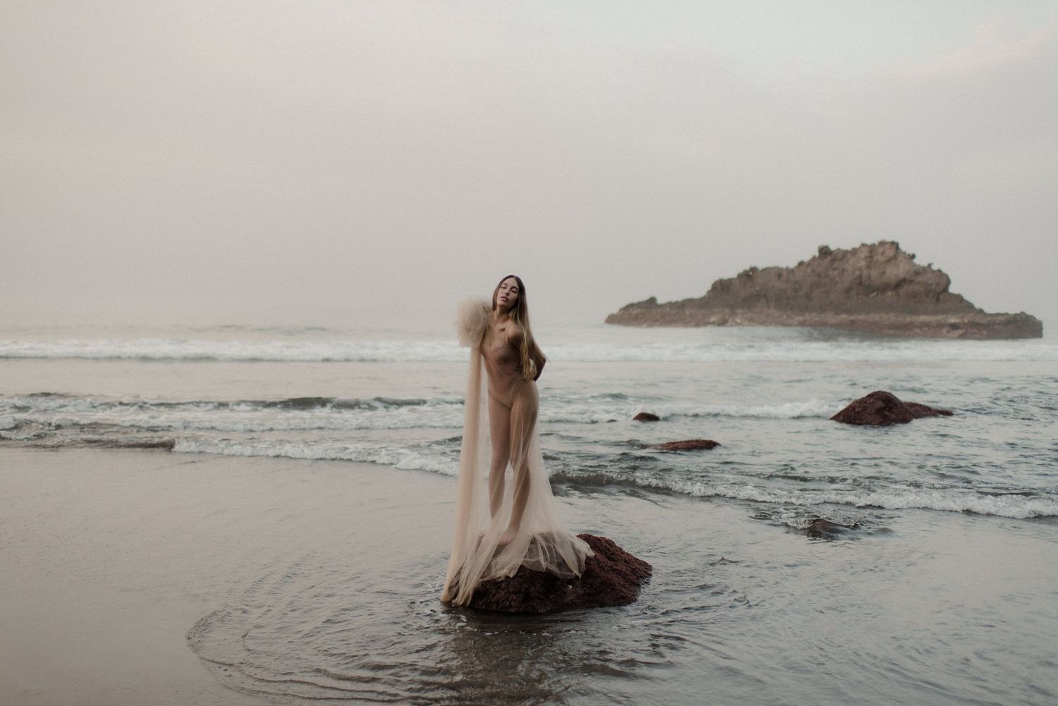 Ethereal bridal portraits on a misty beach at sunset with flowing dress and natural coastal backdrop.