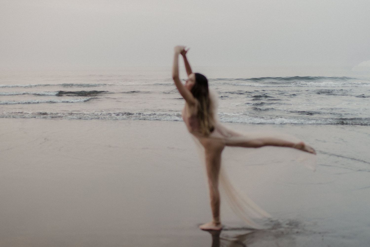Silhouette of a dancer performing graceful movements on a misty beach at dusk.