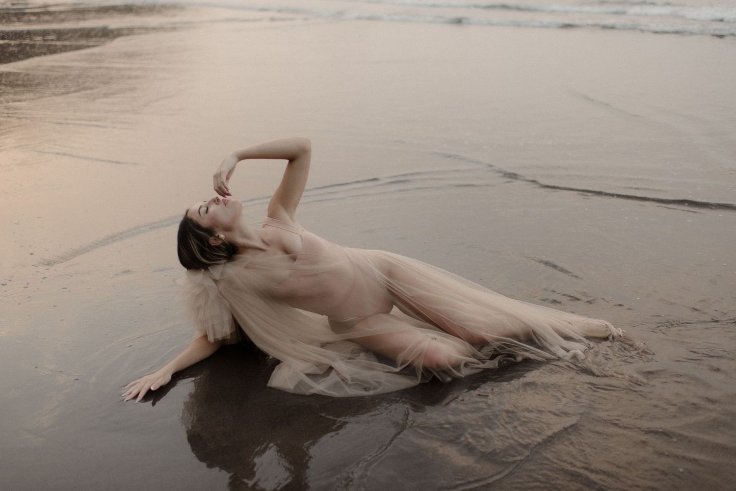 Elegant dance movements performed on sandy shore with waves in background.