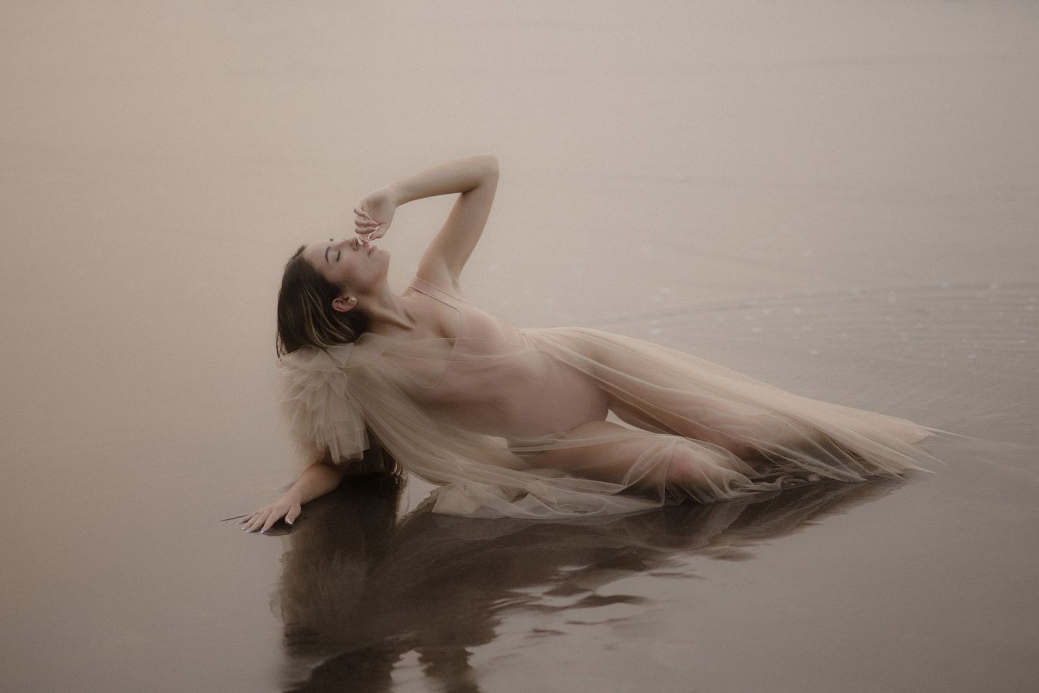Figure floating in water wearing delicate dress creating rippling reflections.