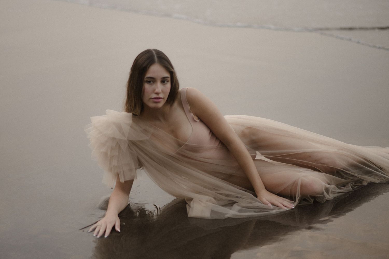 Artistic portrait of figure in pale dress reclining in shallow ocean water.