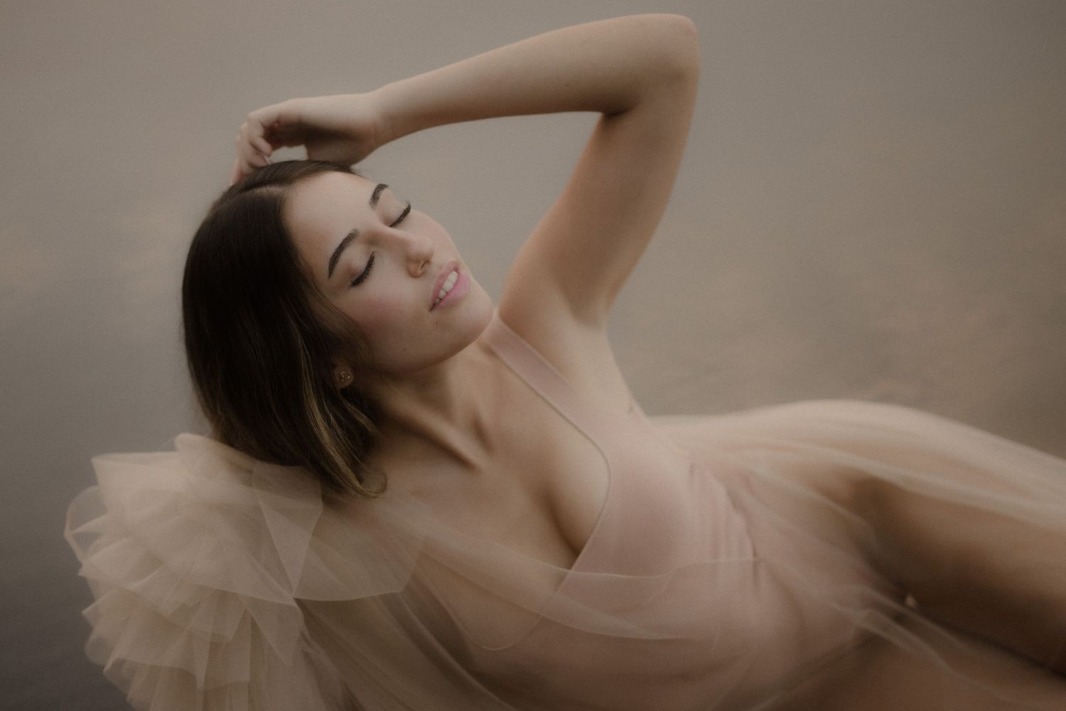 Elegant pose in nude-colored tulle dress against neutral studio backdrop.