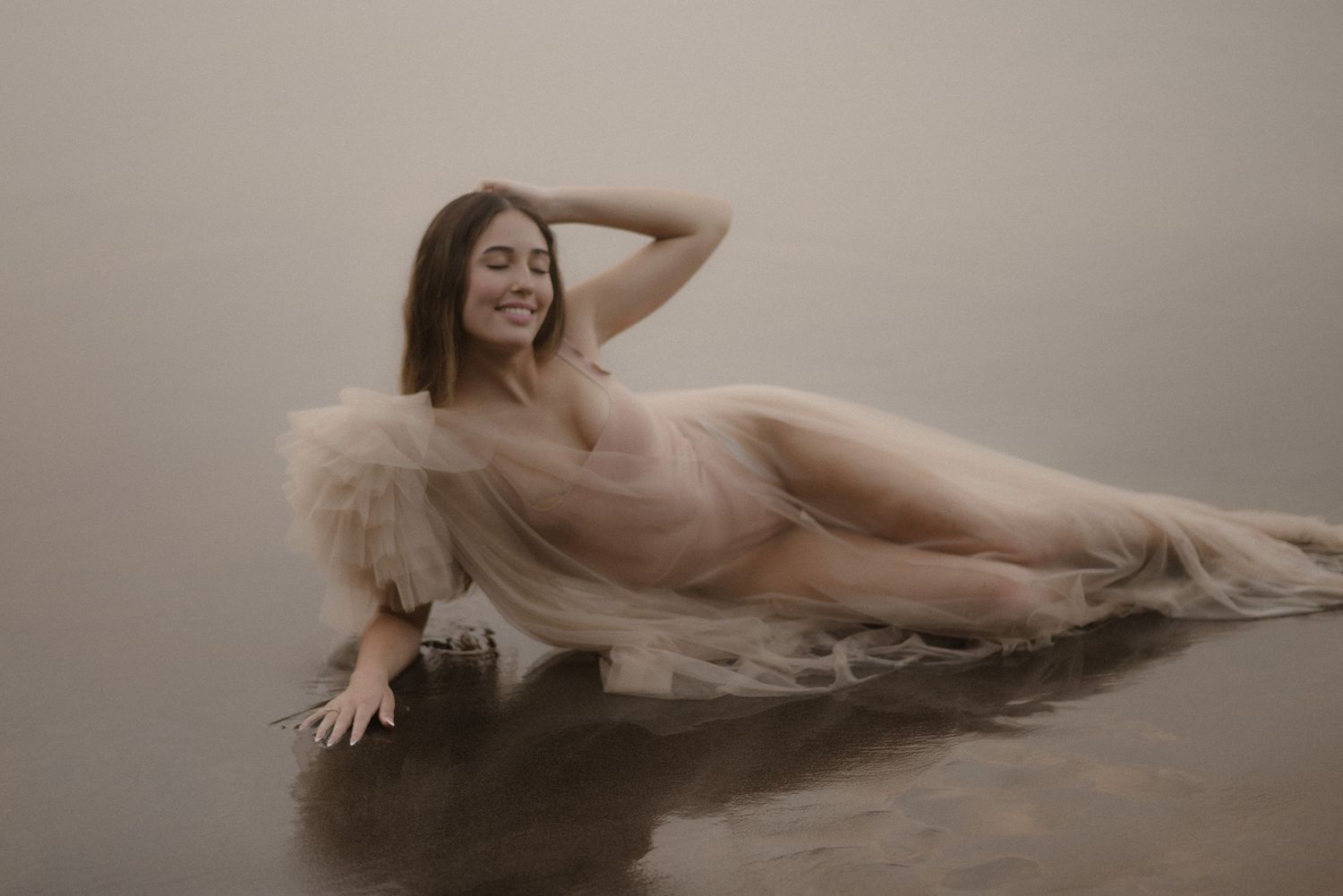 A artistic boudoir photo in foggy water wearing a flowing cream-colored gown.