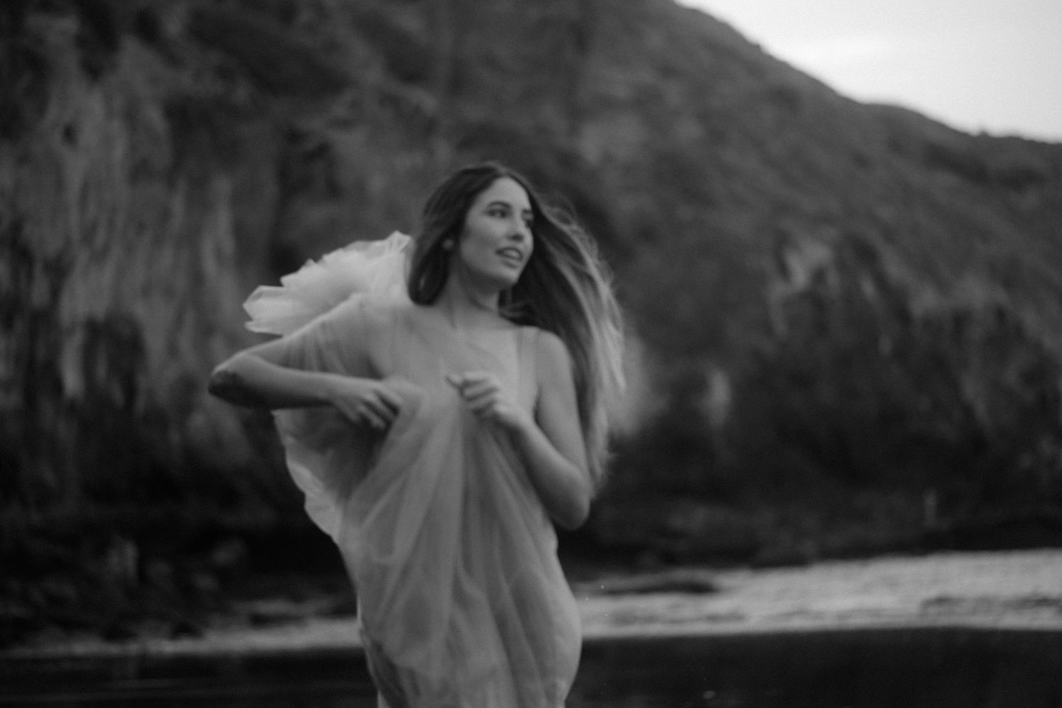 Person in flowy outfit dances joyfully against mountainous landscape.