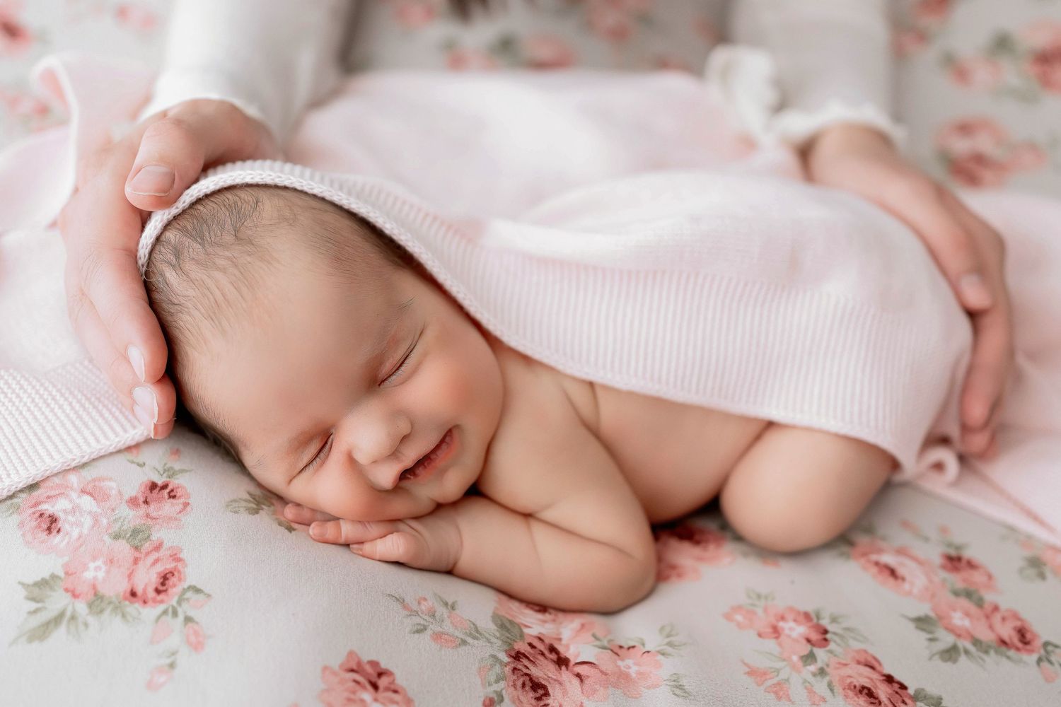 Newborn baby sleeping peacefully on floral pattern fabric with soft pink tones.