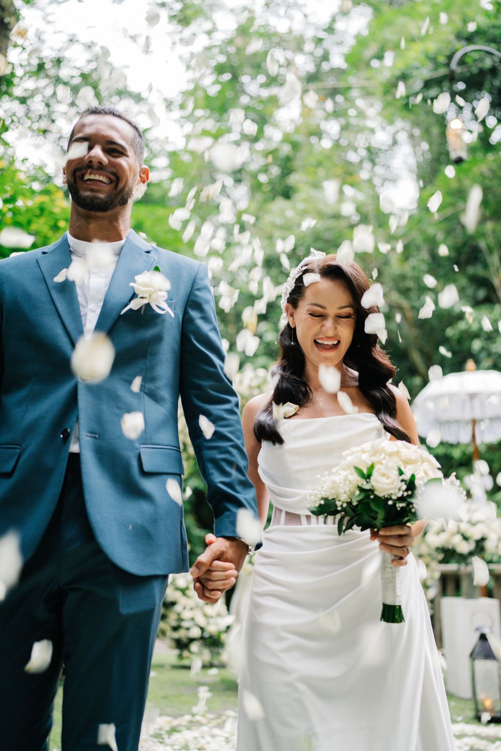 Joyful wedding couple celebrating outdoors with confetti and laughter in a garden setting.