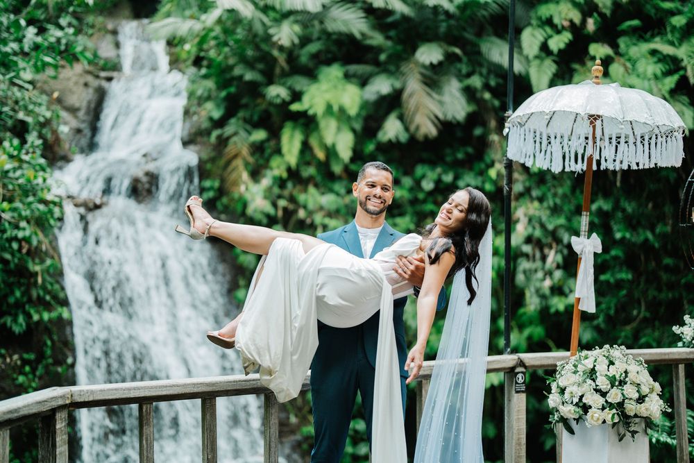 Elegant wedding couple shares tender moments on a deck with tropical foliage and waterfall views.
