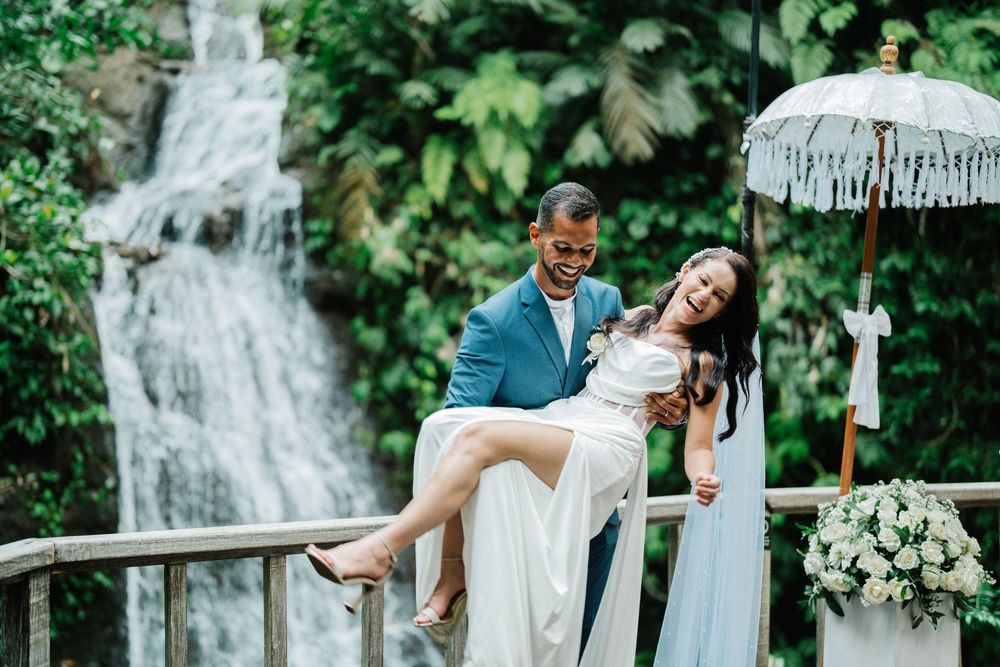 Wedding couple shares playful dip poses on wooden deck surrounded by tropical scenery.