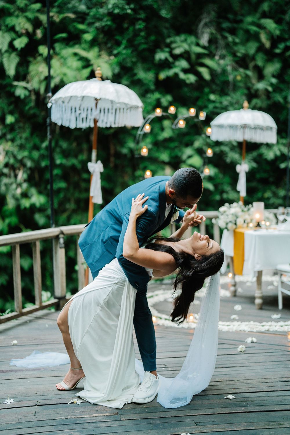 Romantic dip kiss sequence during wedding photoshoot on wooden deck with white decor.