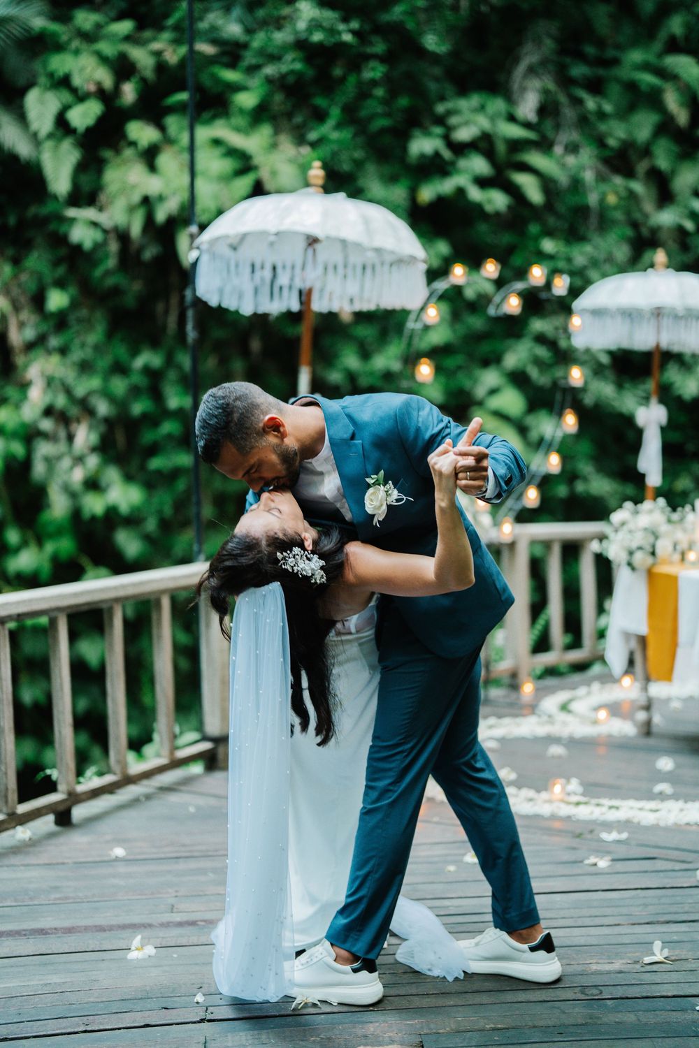 A romantic dip pose between a couple in formal attire on a wooden deck surrounded by greenery.