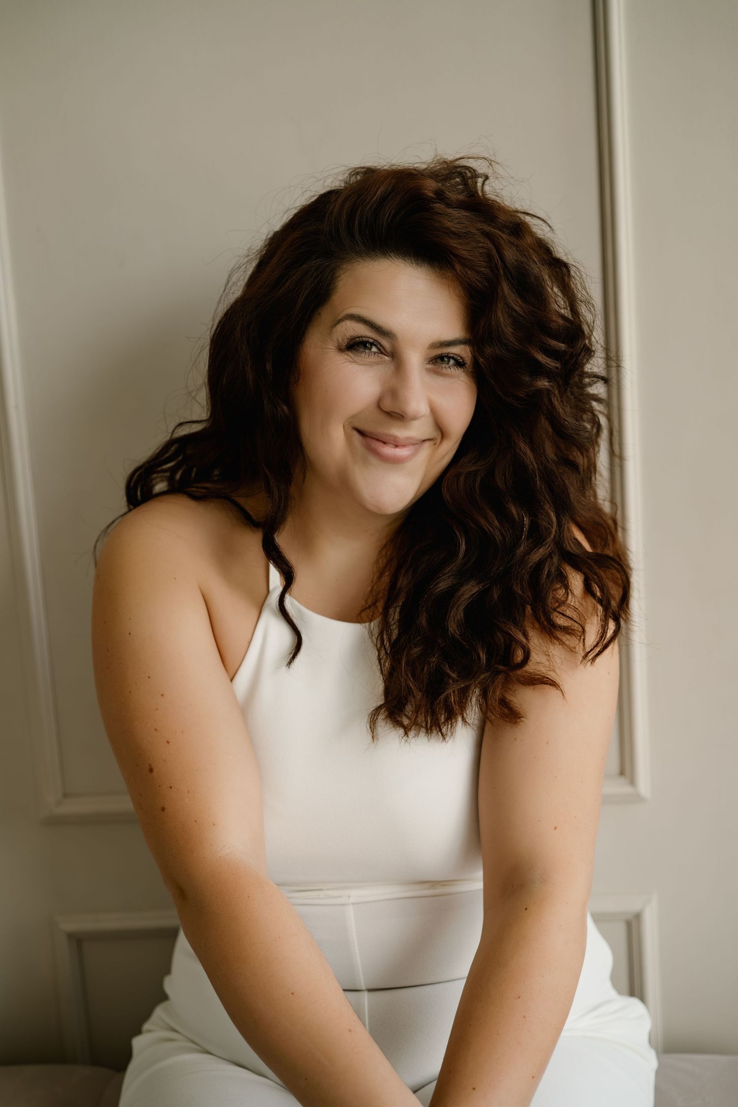 A series of four portrait photos showing someone with wavy dark hair wearing a white sleeveless top against a light background.