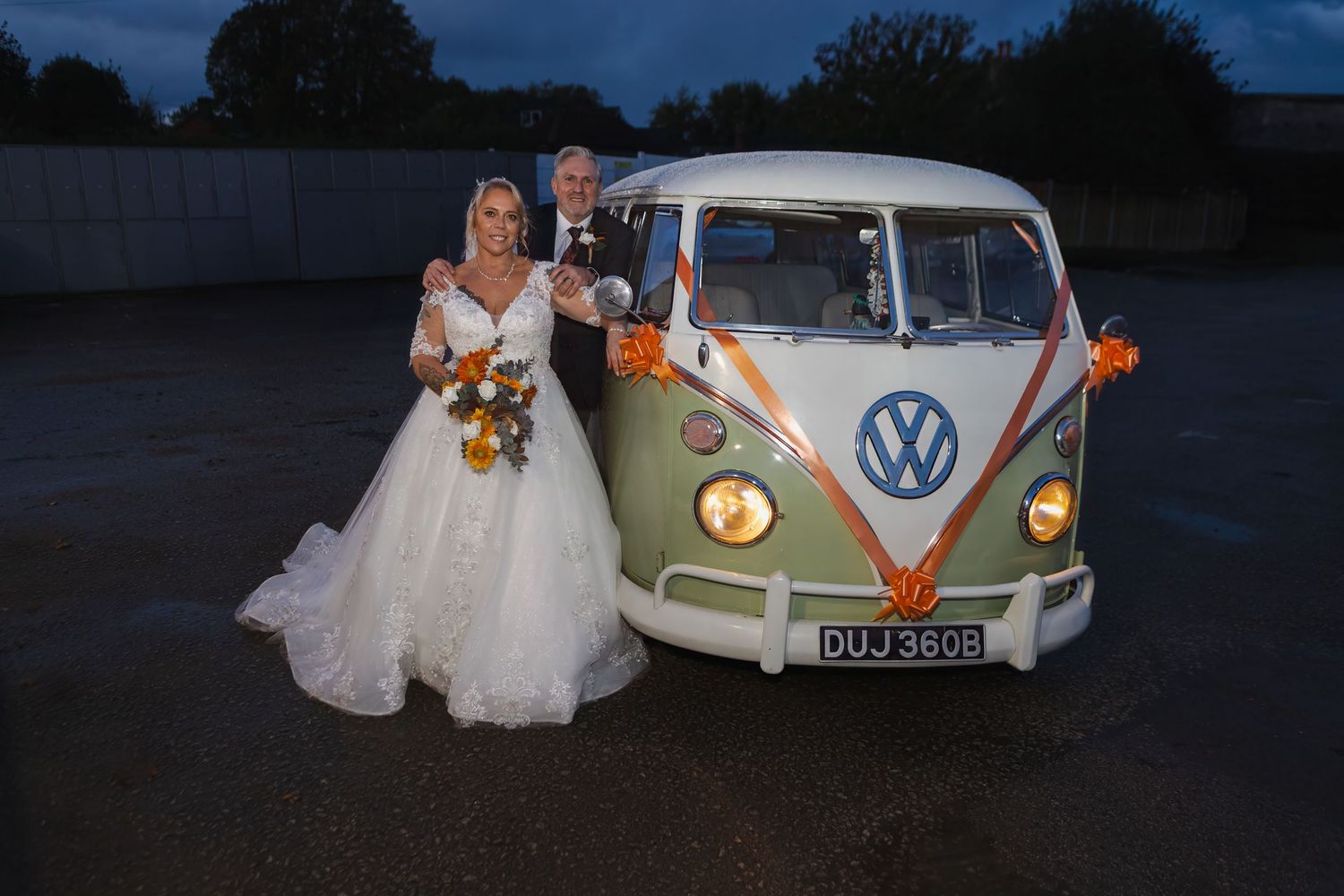 Classic white Volkswagen bus decorated with flowers serves as vintage wedding transportation at dusk.