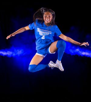 Tennis player in blue uniform leaps dramatically through smoky blue-lit studio space.