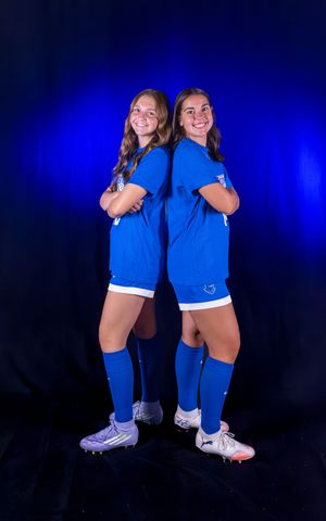 Two athletes in blue soccer uniforms pose together with matching cleats.
