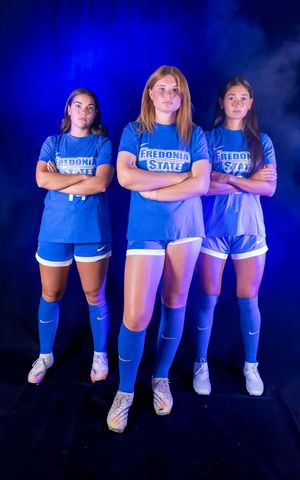 Team photo of soccer players wearing blue jerseys and knee socks against dark background.