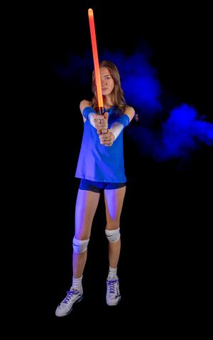 Volleyball player in blue uniform holds an orange glow stick during a dark photo shoot.