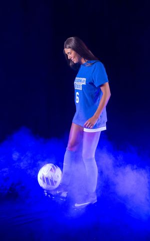 Athletic photoshoot featuring soccer players in blue uniforms with dramatic smoke effects against dark background.