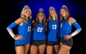 Volleyball team members in blue jerseys pose together for a group photo with dramatic lighting.