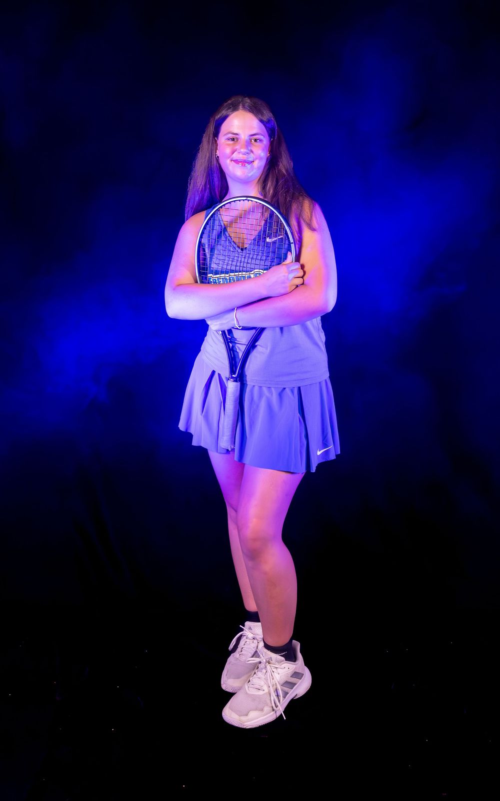 Athletic figure in blue tennis dress strikes dynamic pose with white sneakers against blue backdrop.